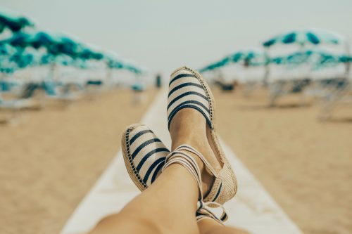 View of woman's legs and feet in espadrille sandals lounging on the beach