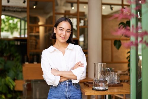 Chân dung cô gái châu Á tươi cười trong chiếc áo sơ mi trắng có cổ làm việc trong quán cà phê
