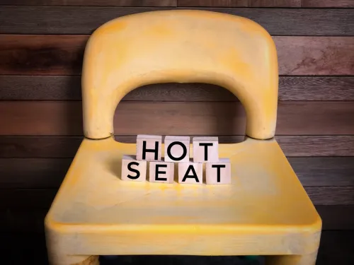'HOT SEAT' word written on wooden blocks and placed on a yellow chair.