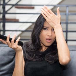 Annoyed young woman watching TV and holding remote control