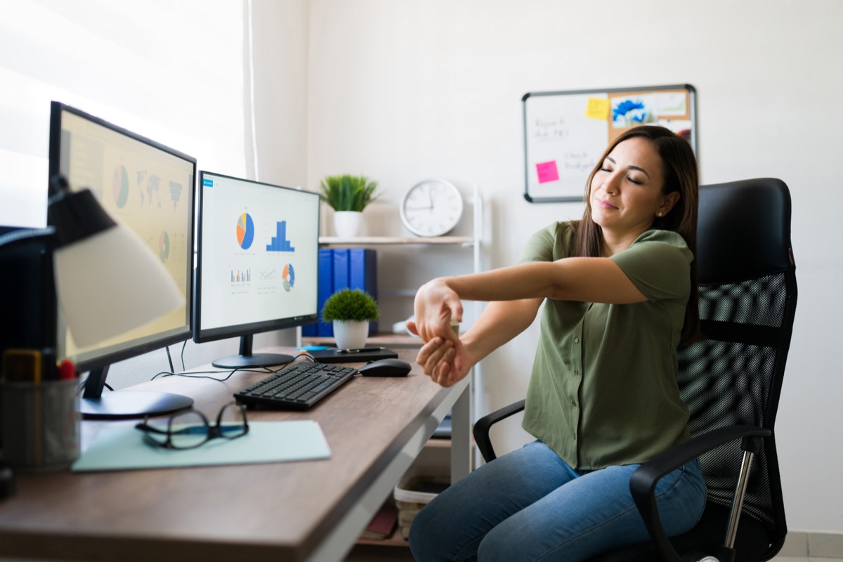 Suffering from carpal tunnel. Attractive young woman stretching her arms and wrists after finishing working on her home desk as a business manager