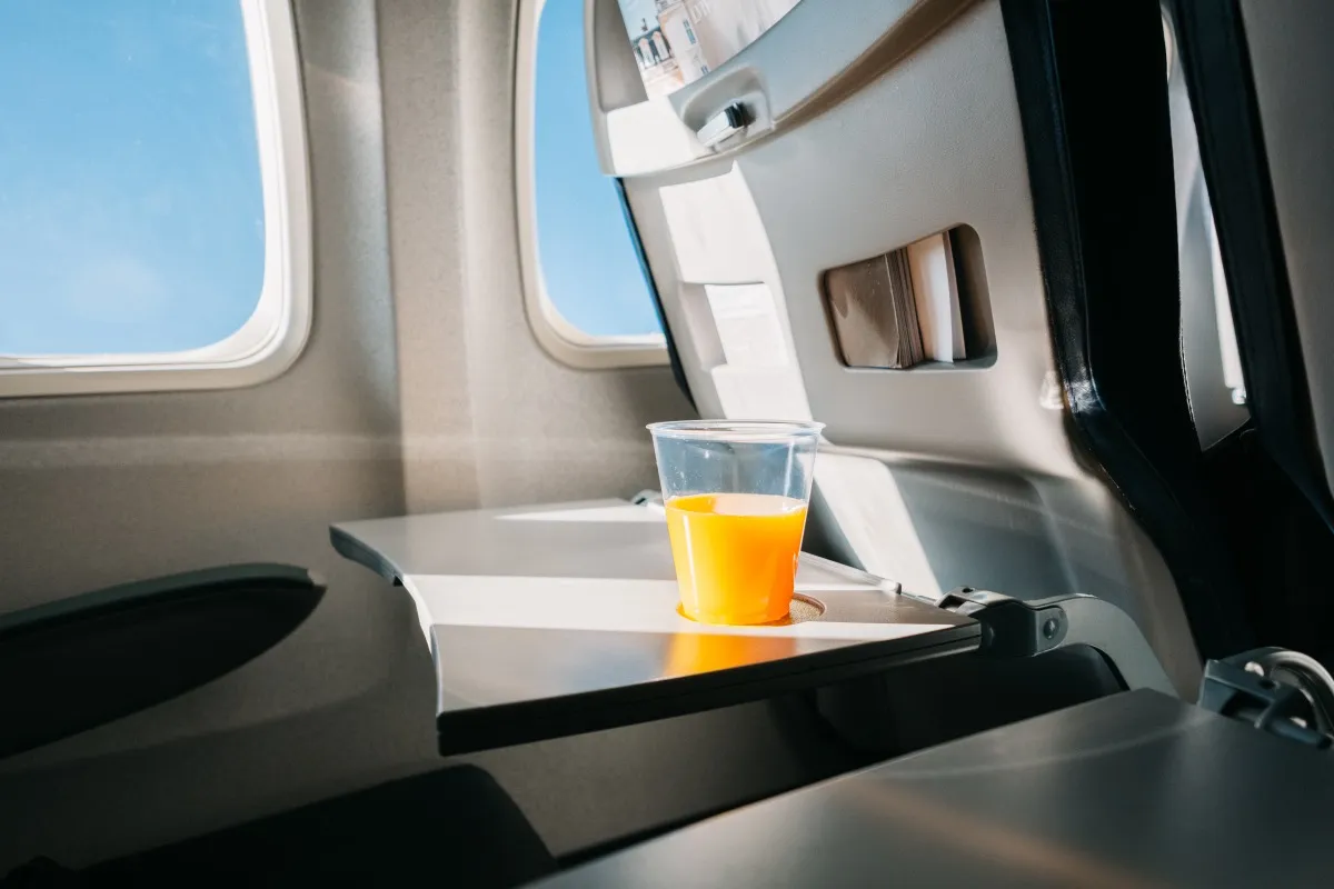 A glass of orange juice on tray table in an airplane. Fine film grain effect
