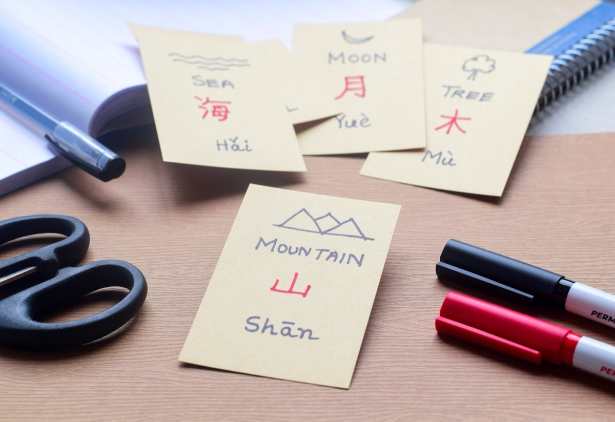 Basic Chinese characters with translation and spelling on flash cards for language learning. Mountain (Shan), Sea (Hai), Moon (Yue) and Tree (Mu). Selective focus.
