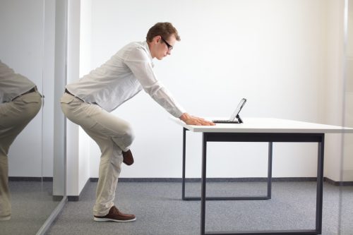Leg stretching during office work - standing man reading at tablet in his office