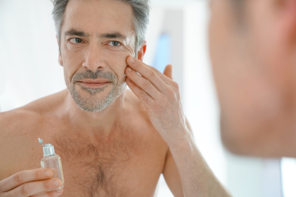 Portrait of mature man in front of mirror applying facial cream