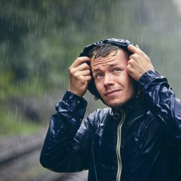 Trip in bad weather. Portrait of young man in drenched jacket in heavy rain.