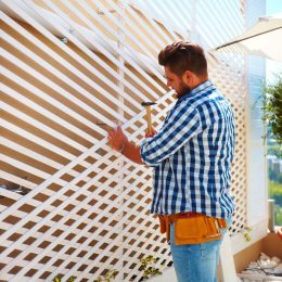 young adult man decorating the house wall, by setting up the wooden trellis for climbing plants