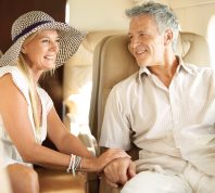Ready for a romantic holiday. Smiling senior couple holding hands on an airplane heading overseas.