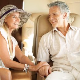 Ready for a romantic holiday. Smiling senior couple holding hands on an airplane heading overseas.