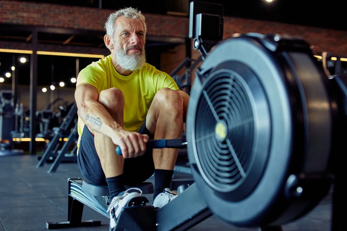 Sport and fitness after 50. Strong mature athletic man in sportswear exercising on rowing machine at gym