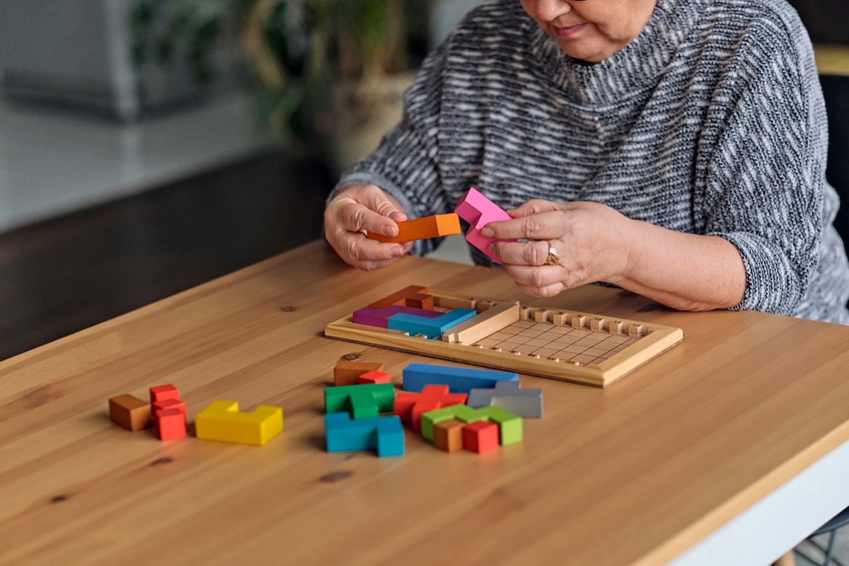 Activity can improve brain function. Elderly woman sitting at table and sorting jigsaw puzzle pieces, free space game