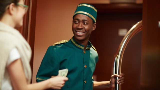 Young guest of hotel giving porter money for his help