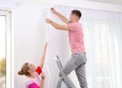 Young couple hanging window curtain indoors. Interior decor element