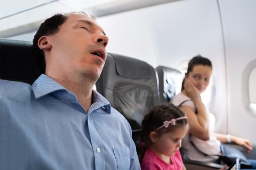 Annoyed Woman Looking At Her Husband Snoring Loud While Sleeping In Airplane