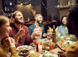 Group of emotional young people enjoying dinner party with friends and smiling happily sitting at table in dimly lit room, copy space