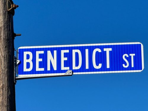 White text on vibrant blue background Benedict St. street sign on utility pole with deep blue sky background.