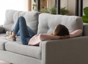 Millennial girl lying and relaxing on comfortable couch after hard work day. Young calm female student having rest, daydreaming, refreshing in living room at home, lazy weekend peace of mind concept.