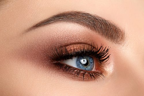 Close up of blue woman eye with beautiful brown with red and orange shades smokey eyes makeup.