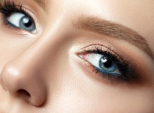 Close up view of blue woman eye with beautiful golden shades and black eyeliner makeup.