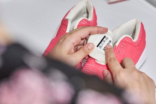 A person cleans and cares for tennis and athletic shoes. Woman checking care label on shoes. Female reading the label of pink sport shoes before putting into automatic washing machine