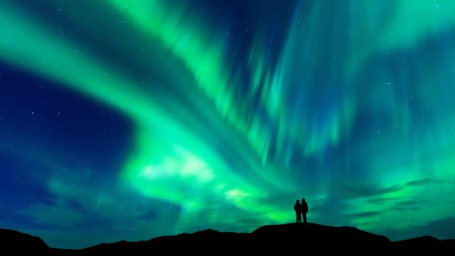 A couple looking up at the Aurora Borealis or Northern Lights.