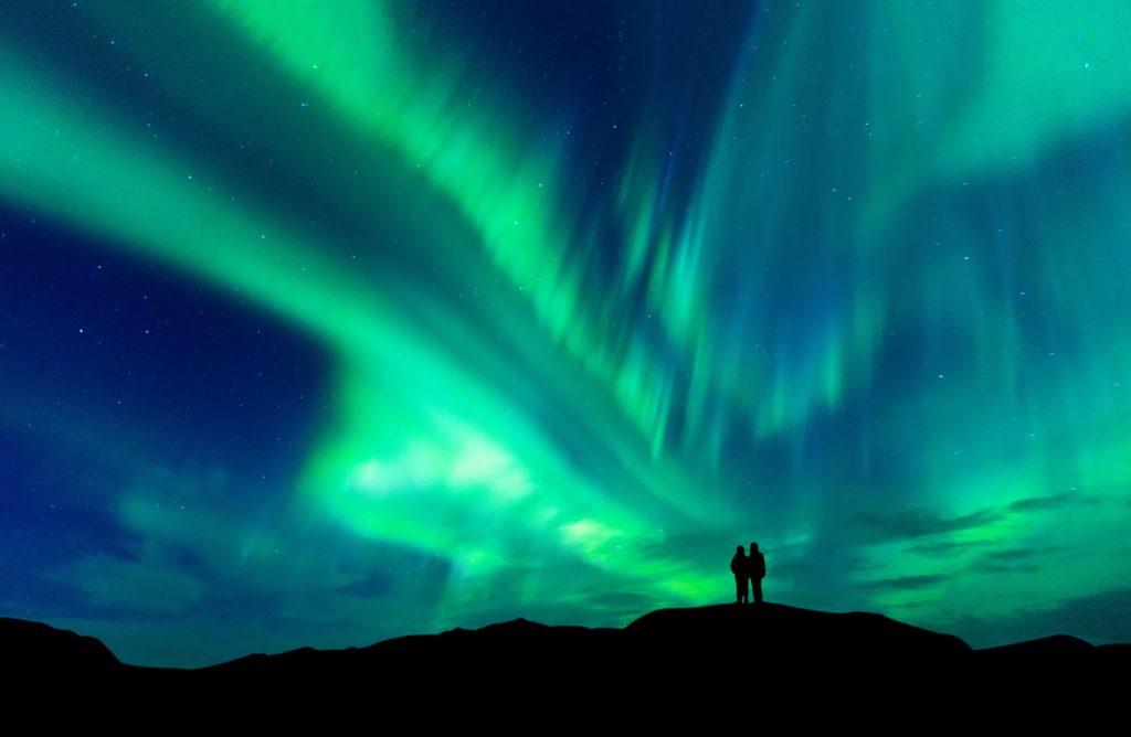 A couple looking up at the Aurora Borealis or Northern Lights.