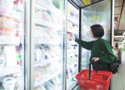 A girl with a basket takes frozen foods from the supermarket's refrigerator. The girl chooses goods in the store. Shopping in the supermarket.