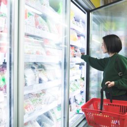 A girl with a basket takes frozen foods from the supermarket's refrigerator. The girl chooses goods in the store. Shopping in the supermarket.