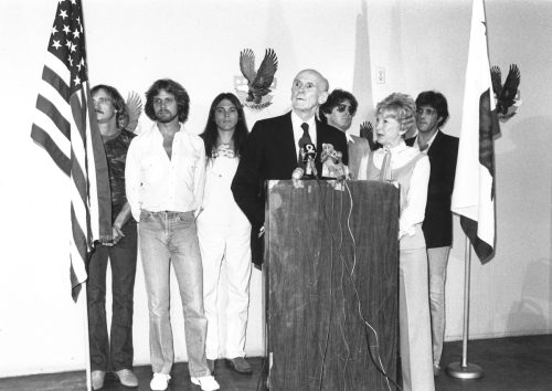 The Eagles standing behind a podium with Alan Cranston and Norma Weintraub in 1980