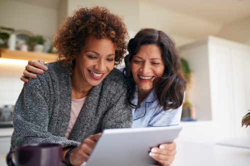 Female couple smiling in their kitchen looking at a tablet