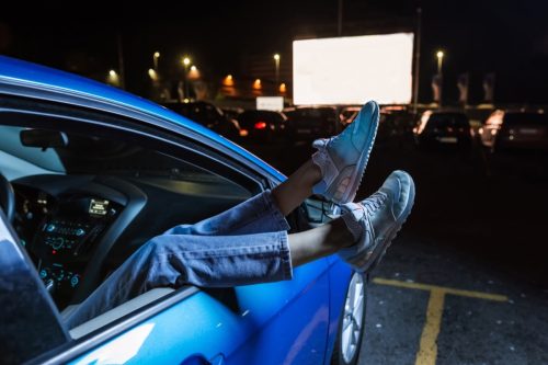 woman hanging her legs out of car window while watching a movie at drive in cinema