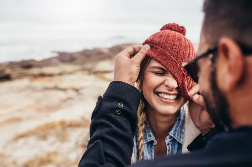Man pulling smiling woman's beanie over her eyes.