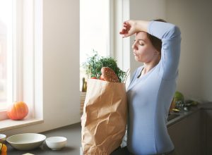 Shot of a young woman looking tired while unpacking fresh produce from a paper bag in the kitchen at home