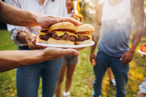 Man holding plate of grilled hamburgers and handing them over to other guests at a barbecue