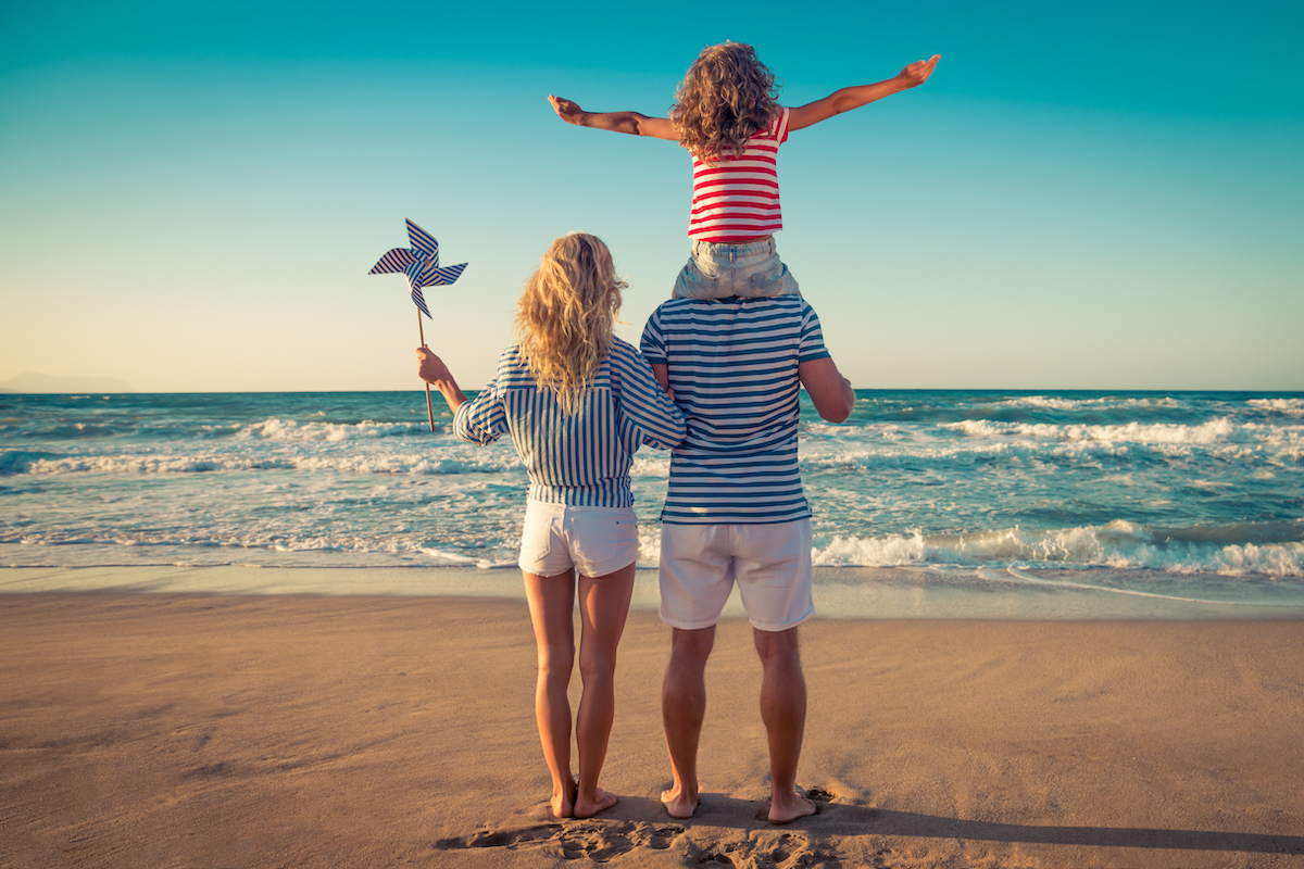 Rear view of a father, mother, and child on a beach wearing red, white, and blue