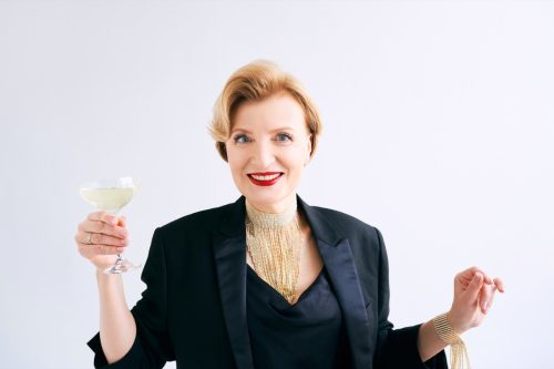 older woman wearing tuxedo style suit holding drink