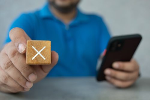 Man showing a rejection sign in wooden cube and holding smartphone. Concept of negative decision making or choice of vote.
