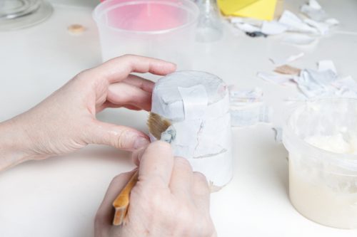 Making papier mache. Female hands with a brush glue a torn paper blank