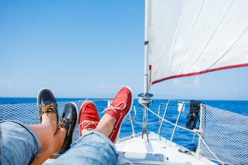 Pairs legs of man and woman legs in red and blue topsiders on white yacht deck.