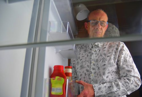 Portrait of a hungry man looking for food in refrigerator. Eating and diet concept - confused middle-aged man looking for food in empty fridge at kitchen.