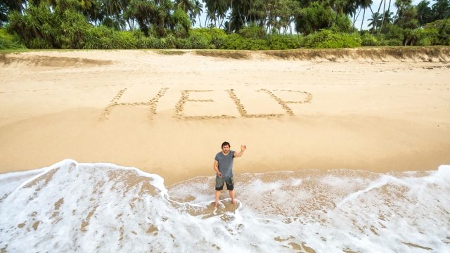 Aerial view of a man stuck on a desert island who wrote "HELP" in the sand