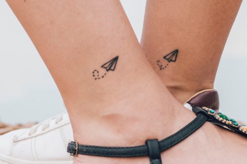 Two friends having the same paper airplane tattoo on their ankles.
