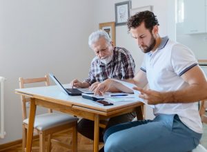 Son Giving Senior Parent Financial Advice at Home. Adult Son Doing Accounts Together With His Senior Father at Home, Planning New Purchase. Family Budget and Finances.