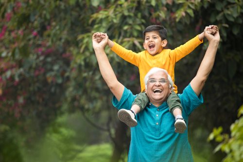 Carefree grandfather carrying grandson on shoulders at park