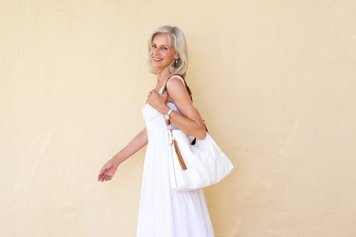 Portrait of happy older woman in summer dress walking with purse