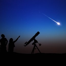 A silhouette of a parent and child watching a shooting star next to their telescope