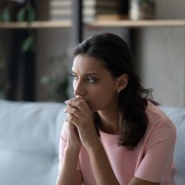 Pensive young Indian woman sitting on a sofa looking off in the distance