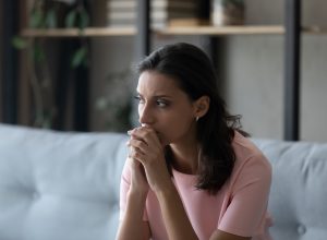 Pensive young Indian woman sitting on a sofa looking off in the distance