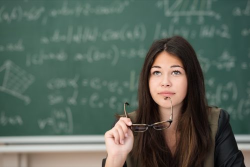 Young woman sitting in front of chalkboard, holding her glasses to her chin