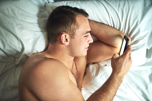 man receiving a sext message in bed